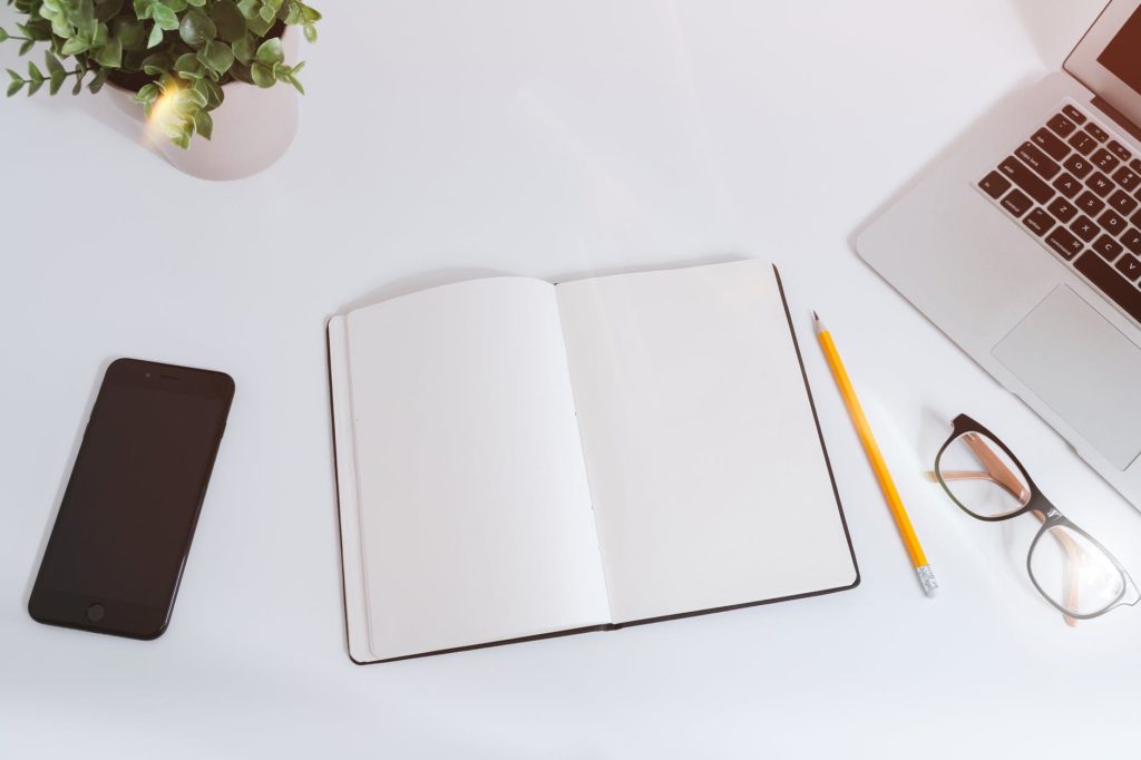 Notebook, laptop, phone, and glasses on a clean desk